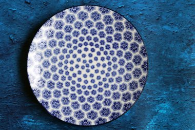 Blue ceramic plate with beautiful pattern. Dark blue textured background with copy space. Modern tableware close up photo. 