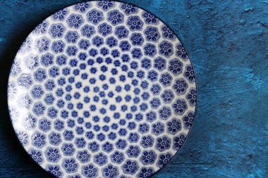 Blue ceramic plate with beautiful pattern. Dark blue textured background with copy space. Modern tableware close up photo. 