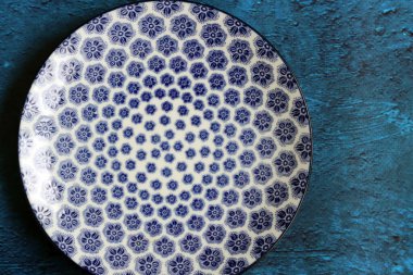 Blue ceramic plate with beautiful pattern. Dark blue textured background with copy space. Modern tableware close up photo. 