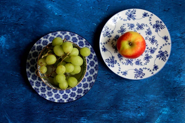 Fruit on a blue decorative crockery. Close up photo of beautifully patterned tableware. Textured backdrop with copy space.