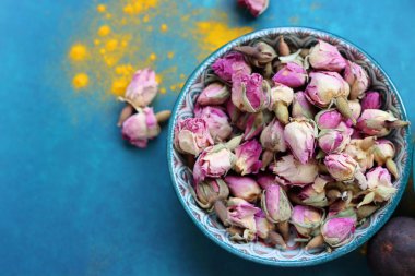 Kurumuş gül tomurcukları yakın plan fotoğraf. Mavi bir seramik kasede gül çiçekleri. Kopyalama alanı olan mavi arkaplan. 