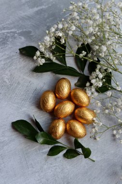 Altın folyoya sarılı çikolatalı Paskalya yumurtası. Beyaz bahar çiçekleri ve Ester şekerlemeleri. Parlak bahar hala hayat. 