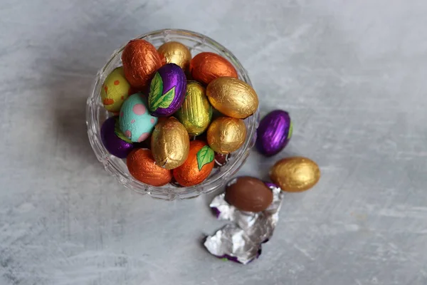 Foil wrapped Easter chocolate eggs in a glass bowl. Easter celebration concept. Colorful still life with sweets. Textured background with copy space. Easter greeting card.