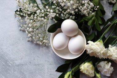Basit kompozisyon. Yumurtalar ve beyaz çiçeklerle hayat devam ediyor. Paskalya kutlaması. Beyaz seramik kasede yumurtalar. Kopyalama alanı olan parlak doku arkaplanı. 