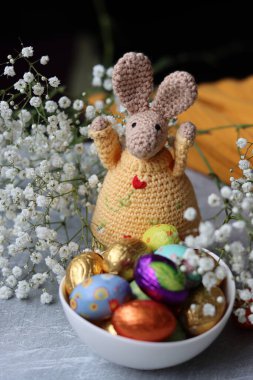 Tığ işi tavşan ve masada bir kase Paskalya tatlısı. Çikolatalı yumurtalar, çiçekler ve oyuncaklarla dolu renkli bir hayat. Paskalya kutlaması kavramı. 