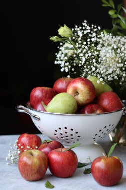 Beyaz metalik kevgire organik armutlar ve elmalar. Sehpadaki mevsimlik meyvelerin fotoğrafını çek. Elmalar ve çingene çiçekleriyle dolu renkli bir hayat. Doğal vitaminler ve antioksidan konsepti. 