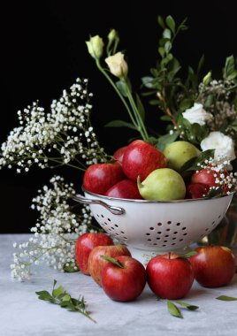 Elmalar ve çiçekler masada. Kevgirde parlak kırmızı elmalar, siyah arkaplan. 