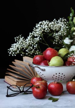 Elmalar ve çiçekler masada. Kevgirde parlak kırmızı elmalar, siyah arkaplan. 