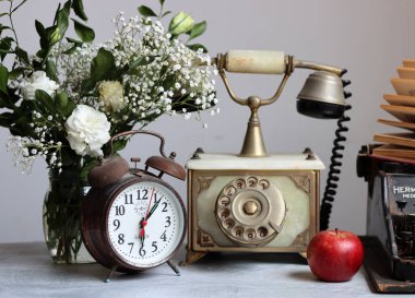 Antika telefon, paslı çalar saat, masanın üstünde kırmızı elma çiçekleri. Kopyalama alanı olan beyaz arkaplan. Retro nesneler natürmort. 