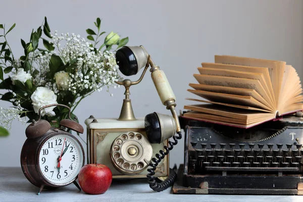 stock image Vintage phone, rusty alarm clock, red apple gypsophila flowers on a desk. White background with copy space. Retro objects still life photo. 