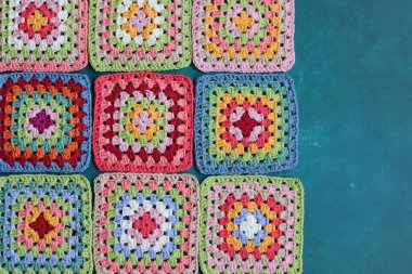 Mavi arka planda büyükanne kareleri. Kopyalama alanı olan üst görünüm. El yapımı tığ işi, örgü işi ve el işi konsepti - tığ işi aksesuarlar