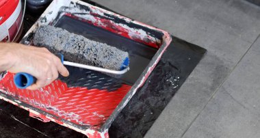 Ressamın aletleri fotoğrafı kapatır. Duvarı boya rulosuyla boyama sürecinde olan bir işçi. Gri bir arkaplanda, yakın plan boya silindiri