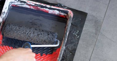 Ressamın aletleri fotoğrafı kapatır. Duvarı boya rulosuyla boyama sürecinde olan bir işçi. Gri bir arkaplanda, yakın plan boya silindiri