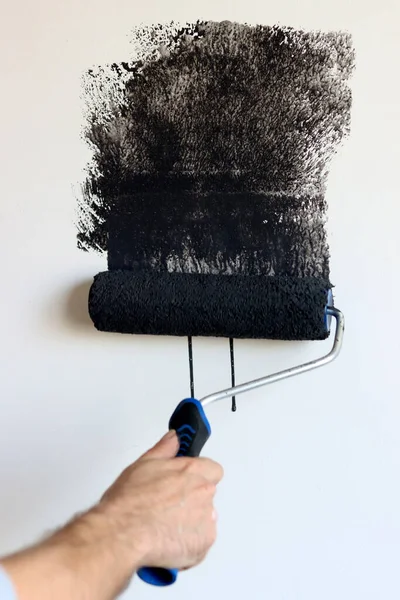 stock image Painter paints the wall with black paint, close-up. Home renovation concept. Male hand holding paint roller. 