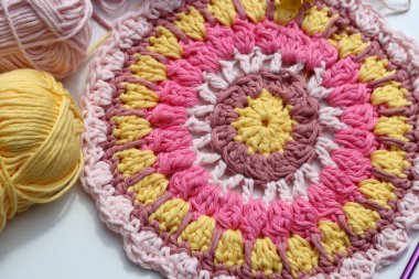 Beyaz masa üzerinde çiçekler olan renkli yuvarlak örgü desenli. Uzayı metin için kopyala. El yapımı Mandala deseni. Sanat ve hobiler kavramı. 