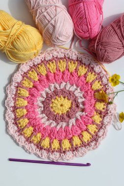 Beyaz masa üzerinde çiçekler olan renkli yuvarlak örgü desenli. Uzayı metin için kopyala. El yapımı Mandala deseni. Sanat ve hobiler kavramı. 
