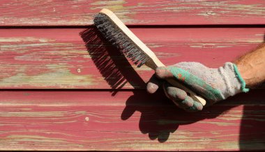 Eldiven giyen erkek, tahta duvarın boyasını tel fırça boyası silici kullanarak çıkarıyor. Yenileme konsepti. 