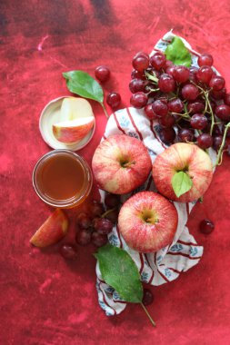 Sonbahar, kırmızı desenli arka planda olgun elma ve üzümlerle dolu bir hayattır. Üst görünüm.