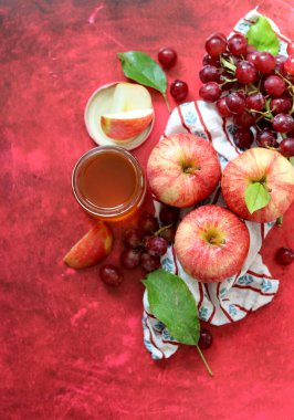 Sonbahar, kırmızı desenli arka planda olgun elma ve üzümlerle dolu bir hayattır. Üst görünüm.