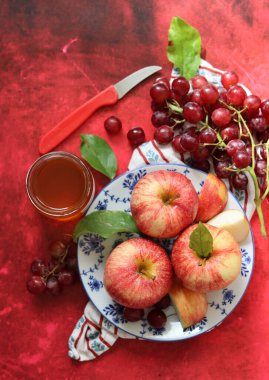 Sonbahar, kırmızı desenli arka planda olgun elma ve üzümlerle dolu bir hayattır. Üst görünüm.
