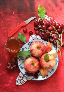 Sonbahar, kırmızı desenli arka planda olgun elma ve üzümlerle dolu bir hayattır. Üst görünüm.