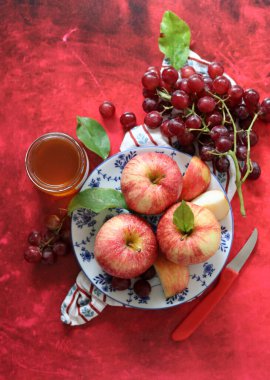 Kırmızı arka planda kırmızı elma ve üzüm ve bir fincan bal. Yahudi yeni yılı Rosh Hashana kutlaması. Mevsimlik meyve ve bal ile sakin bir hayat. 