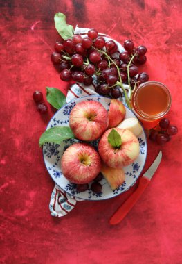 Kırmızı arka planda kırmızı elma ve üzüm ve bir fincan bal. Yahudi yeni yılı Rosh Hashana kutlaması. Mevsimlik meyve ve bal ile sakin bir hayat. 
