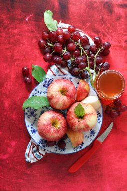 Sonbahar, kırmızı desenli arka planda olgun elma ve üzümlerle dolu bir hayattır. Üst görünüm.