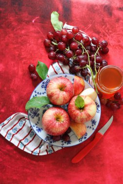 Kırmızı arka planda kırmızı elma ve üzüm ve bir fincan bal. Yahudi yeni yılı Rosh Hashana kutlaması. Mevsimlik meyve ve bal ile sakin bir hayat. 