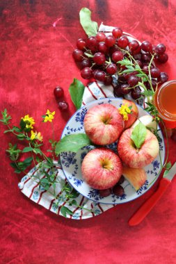 Sonbahar, kırmızı desenli arka planda olgun elma ve üzümlerle dolu bir hayattır. Üst görünüm.