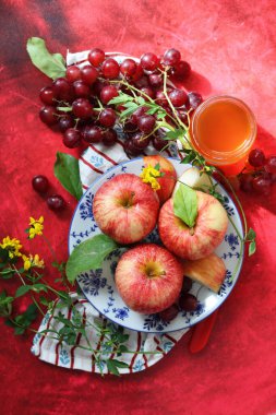 Sonbahar, kırmızı desenli arka planda olgun elma ve üzümlerle dolu bir hayattır. Üst görünüm.