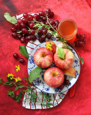 Kırmızı arka planda kırmızı elma ve üzüm ve bir fincan bal. Yahudi yeni yılı Rosh Hashana kutlaması. Mevsimlik meyve ve bal ile sakin bir hayat. 