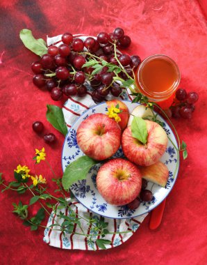 Kırmızı arka planda kırmızı elma ve üzüm ve bir fincan bal. Yahudi yeni yılı Rosh Hashana kutlaması. Mevsimlik meyve ve bal ile sakin bir hayat. 