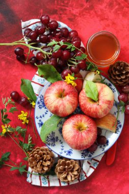 Sonbahar, kırmızı desenli arka planda olgun elma ve üzümlerle dolu bir hayattır. Üst görünüm.