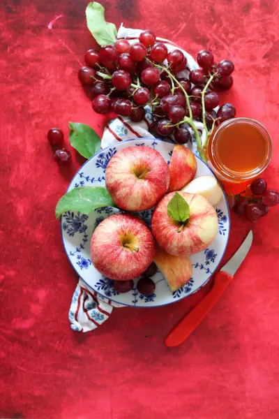 Sonbahar, kırmızı desenli arka planda olgun elma ve üzümlerle dolu bir hayattır. Üst görünüm.