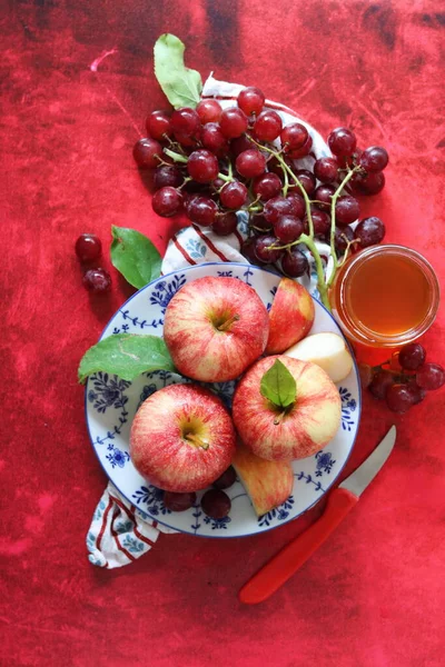 Sonbahar, kırmızı desenli arka planda olgun elma ve üzümlerle dolu bir hayattır. Üst görünüm.