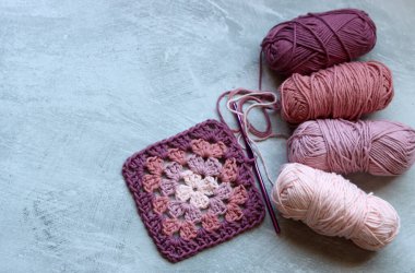 Büyükanne kare örgü deseni. Yumuşak pembe organik ipliğin renkli fotoğrafı. Hobiler ve eğlence konsepti. Kopyalama alanı olan açık gri arkaplan.