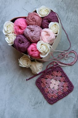 Renkli pamuk toplarından oluşan bir buket kalp şeklinde bir kutuda, arka planda gri bir fotokopi alanı var. Sanat ve zanaat konsepti. 