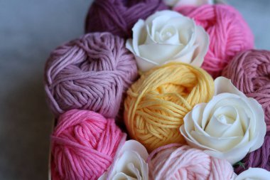 Çok renkli pamuk yumakları ve beyaz güller gri bir arka planda bir sepetin içinde ve yazı için boşluk var. Organik iplikli el yapımı bir hediye kutusu. Tığ işi aşıklar için yaratıcı bir hediye.. 