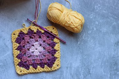 Yumuşak organik pamuktan yapılmış büyükanne kare deseni. Fotokopi alanı olan gri arkaplan. Bahar tığ işi fikirleri. 