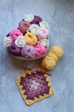 Çok renkli pamuk yumakları ve beyaz güller gri bir arka planda bir sepetin içinde ve yazı için boşluk var. Organik iplikli el yapımı bir hediye kutusu. Tığ işi aşıklar için yaratıcı bir hediye.. 