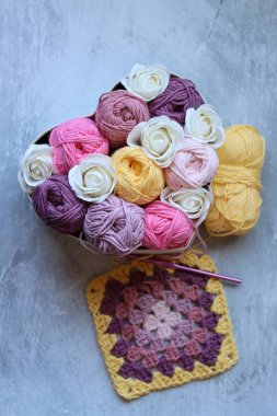 Renkli pamuk toplarından oluşan bir buket kalp şeklinde bir kutuda, arka planda gri bir fotokopi alanı var. Sanat ve zanaat konsepti. 