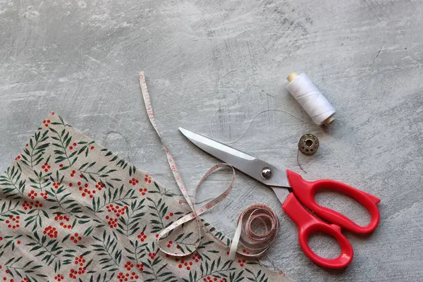 Sewing tools: scissors, thread, fabric, pins, buttons and colorful soft cotton fabric on grey background with copy space Flat lay composition with sewing accessories