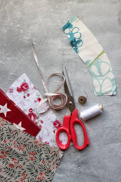 Sewing tools: scissors, thread, fabric, pins, buttons and colorful soft cotton fabric on grey background with copy space Flat lay composition with sewing accessories