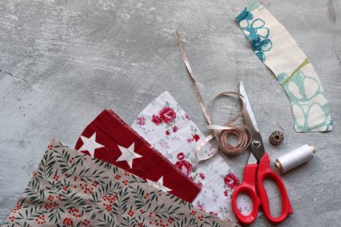 Makas, renkli kumaş, makara, bant, ölçü bandı ve fotokopi hızıyla gri arkaplana kıyafet dikmek için düğmeler. 