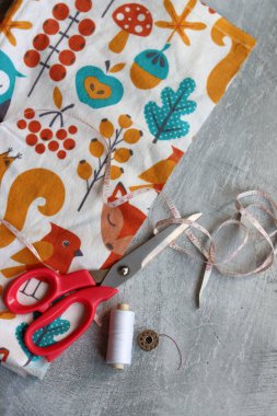 Makas, renkli kumaş, makara, bant, ölçü bandı ve fotokopi hızıyla gri arkaplana kıyafet dikmek için düğmeler. 