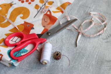 Yumuşak flanel kumaştan bir elbise dikmek, işlem aşamasında. Fotokopi alanı olan gri bir arka planda dikiş aletleri ve aksesuarları dikiyorum. Hobiler ve el sanatları konsepti. 