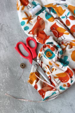 Yumuşak flanel kumaştan bir elbise dikmek, işlem aşamasında. Fotokopi alanı olan gri bir arka planda dikiş aletleri ve aksesuarları dikiyorum. Hobiler ve el sanatları konsepti. 