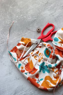 Yumuşak flanel kumaştan bir elbise dikmek, işlem aşamasında. Fotokopi alanı olan gri bir arka planda dikiş aletleri ve aksesuarları dikiyorum. Hobiler ve el sanatları konsepti. 