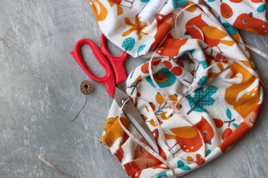 Yumuşak flanel kumaştan bir elbise dikmek, işlem aşamasında. Fotokopi alanı olan gri bir arka planda dikiş aletleri ve aksesuarları dikiyorum. Hobiler ve el sanatları konsepti. 